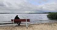 Ein Mann sitzt auf einer Bank am Wasser und schaut hinaus.