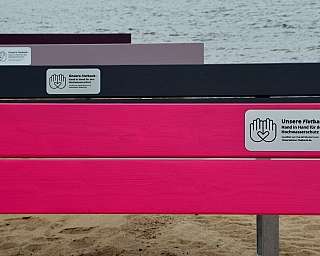 Bunte Bänke mit Schildern zum Hochwasserschutz am Strand.